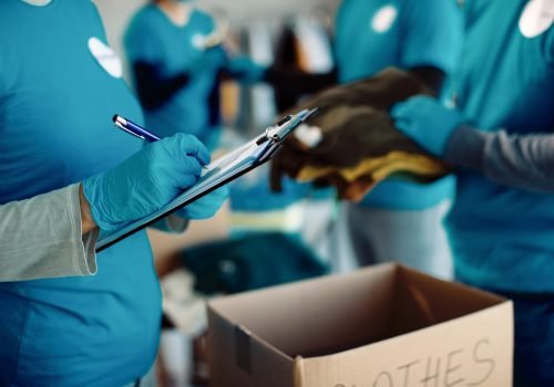 Close-up of woman taking notes while volunteers are packing donation boxes for charity.