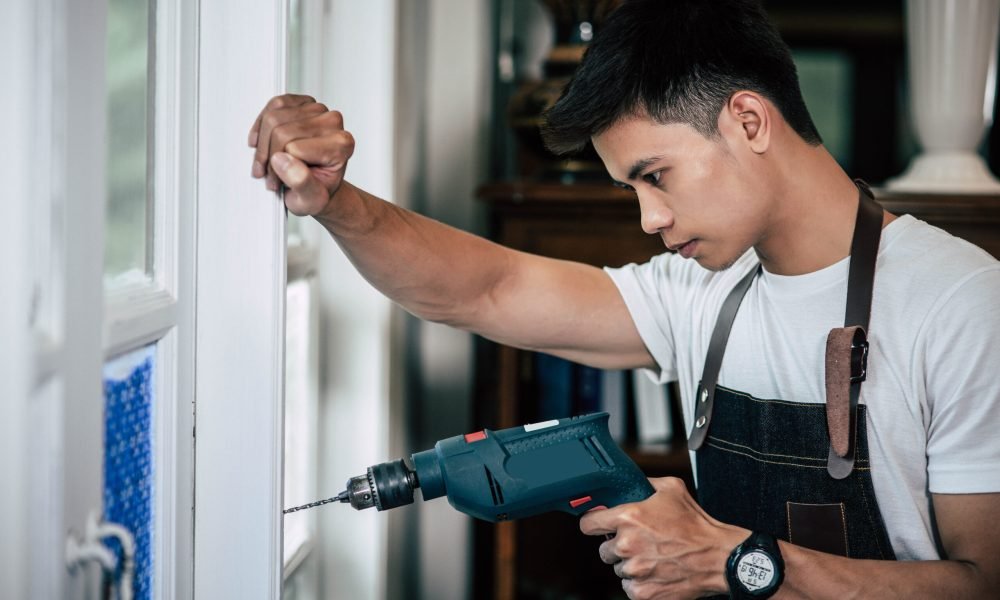 The carpenter holds the drill and drills the window. Selective focus.
