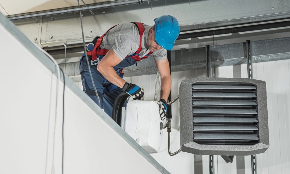 Caucasian HVAC Technician Worker in His 40s Installing Air and Water Heaters Inside Newly Constructed Warehouse.